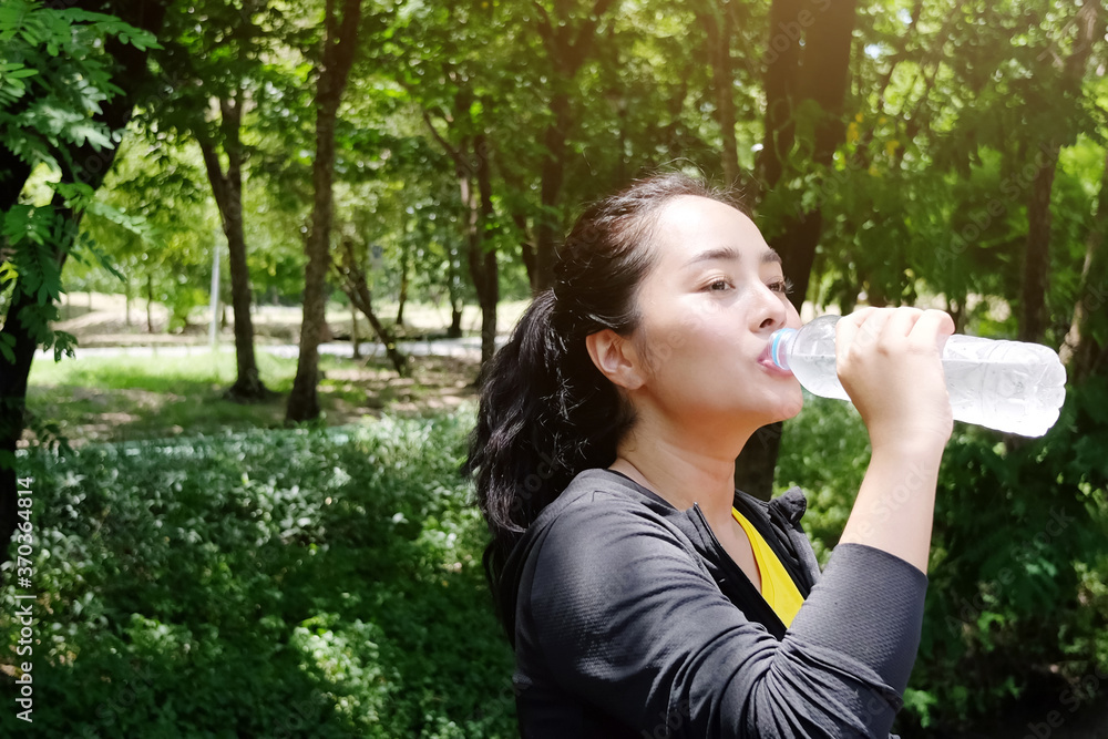 Asian young woman in black and yellow sportwear Thirsty and and drinking water in bottle after exercise and running with natural sunlight in the garden. Asian young woman in black and yellow sportwear Thirsty and and drinking water in bottle after exercise and running with natural sunlight in the garden.