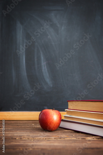 Books and apples on wooden table against the background of the chalkboard or blackboard.
