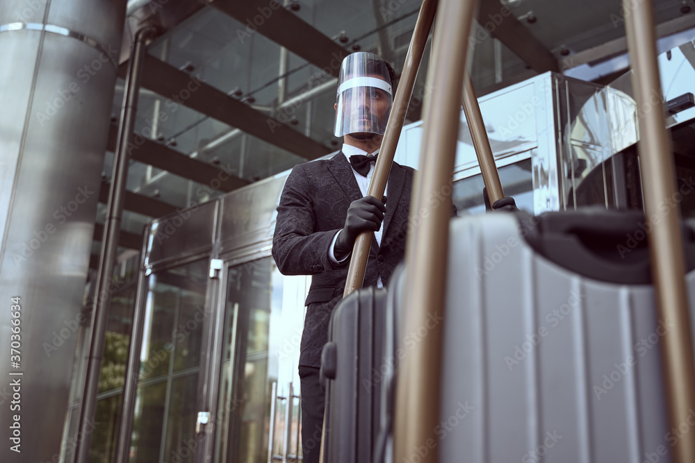 Hotel worker in protective equipment operating a heavy trolley - obrazy, fototapety, plakaty 