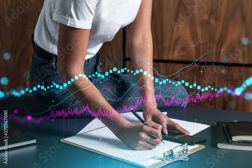 Businesswoman taking notes using smart-phone. Financial forex graph and chart hologram double exposure.