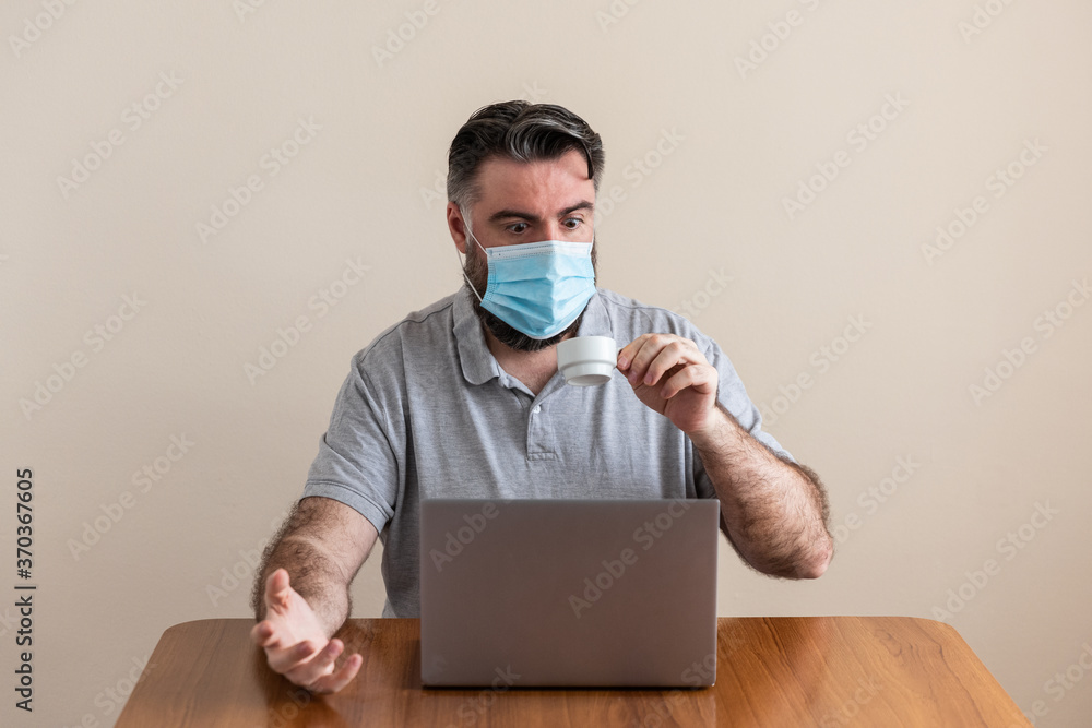 man drinks coffee while wearing a laptop and a mask covid19