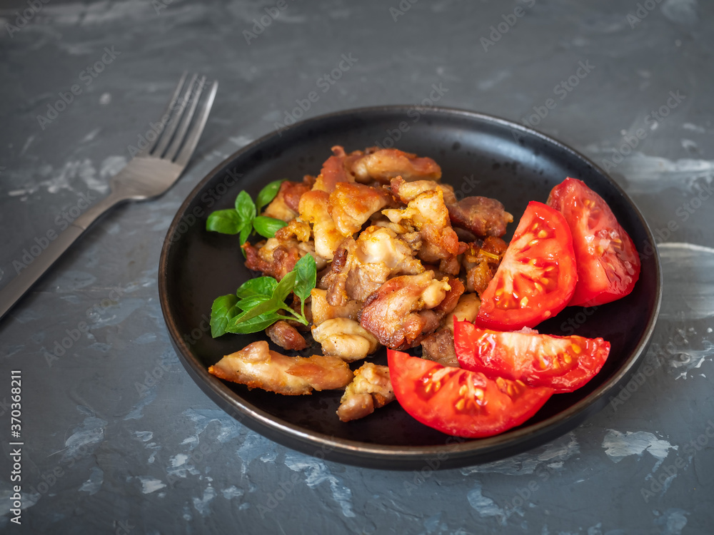 Breakfast with chicken fried fillets and chopped red tomatoes on a round dark plate and basil leaves Breakfast with chicken fried fillets and chopped red tomatoes on a round dark plate and basil leaves