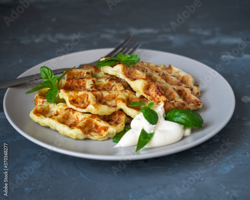 Zucchini shoes with the addition of cheese on a light plate top viewZucchini waffles with sour cream-mushroom sauce and basil leaves on a light plate with a table fork for