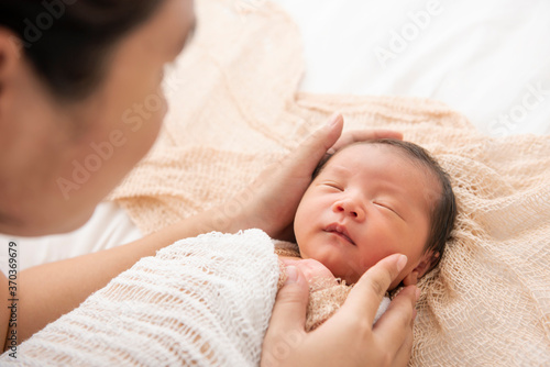 Asian newborn baby sleeping in white blanket and mother hold on hand. portrait of a beautiful asleep infant baby on white.