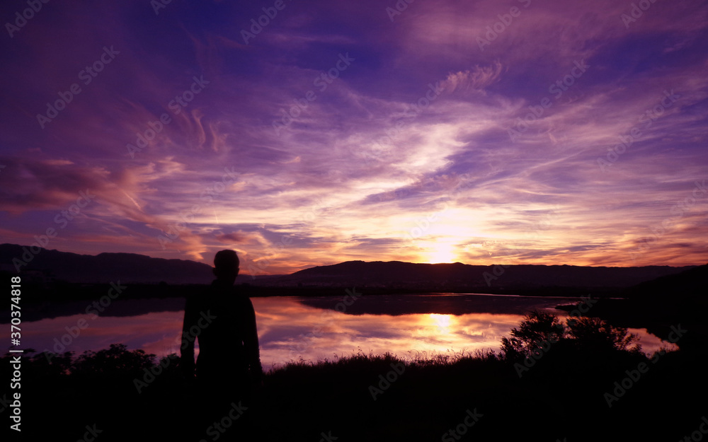 man watching sunset over the river: a stunning sunset with very beautiful sky evening with natural full colors, boy stand up watch the fantastic landscape sunlight reflection 