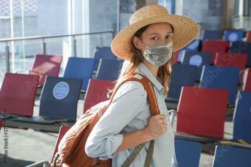 Tourist woman  with protective medical mask and hand luggage waiting for the flight at the airport. Safety measures during coronavirus. New normal concept. © triocean