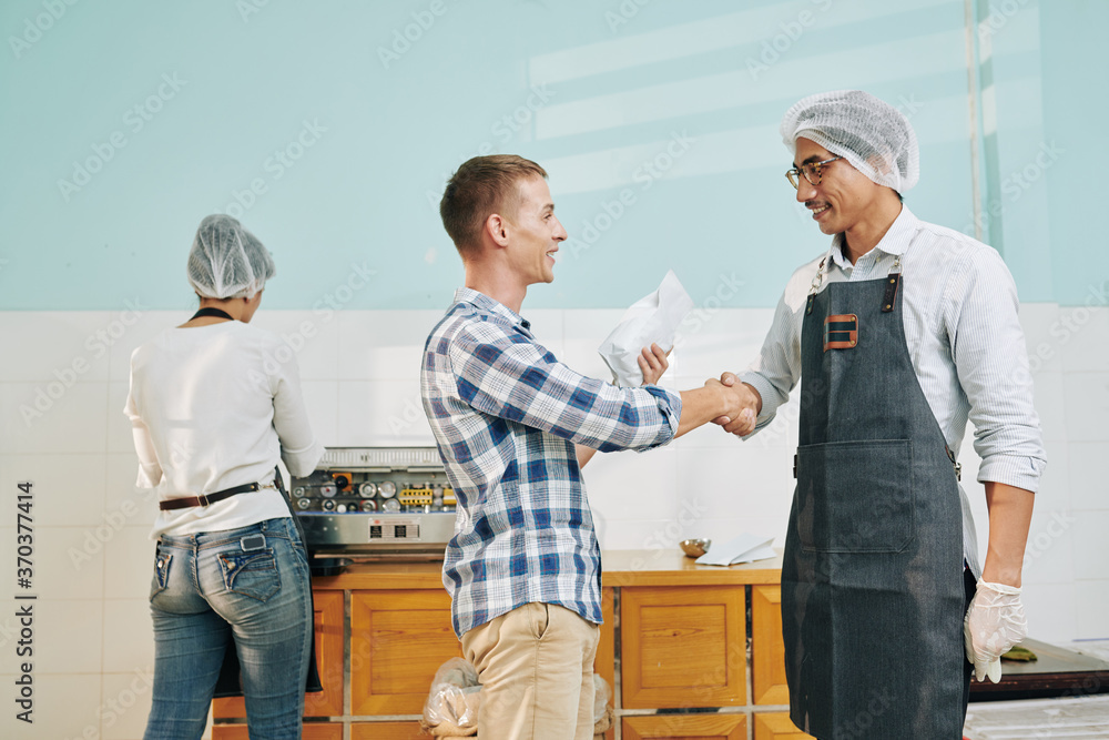 Obraz premium Happy businessman shaking hand of roastery owner after singing contract on selling roasted coffee beans in his shop