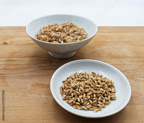 Boiled spelt in a bowl isolated on wooden background with seeds