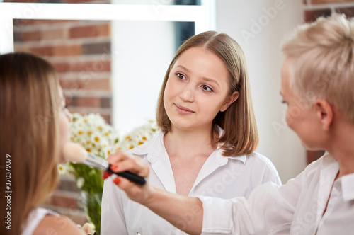 team of professional caucasian makeup artists working with young model. two make-up artist doing make-up in two hands and talk