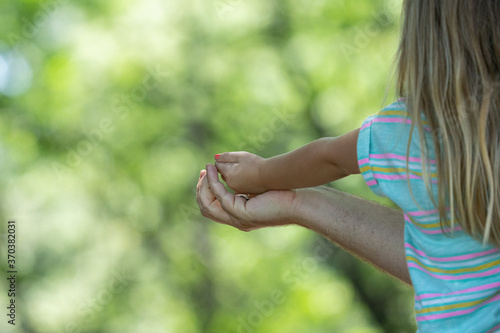 father hold daughters hand to feed birds in the nearby tree