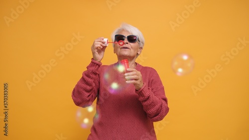 Trendy granny blowing soap bubbles. Studio shot. High quality photo