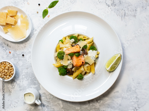 Pasta penne with salmon, broccoli, and pesto sauce on the white-gray background. Flat lay.