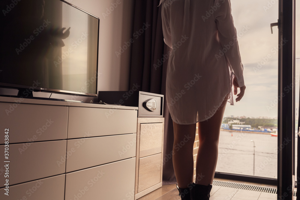 Φωτογραφία Back view of silhouette lonely beautiful young woman in a transparent nightgown standing near curtained panoramic window of skyscraper apartments