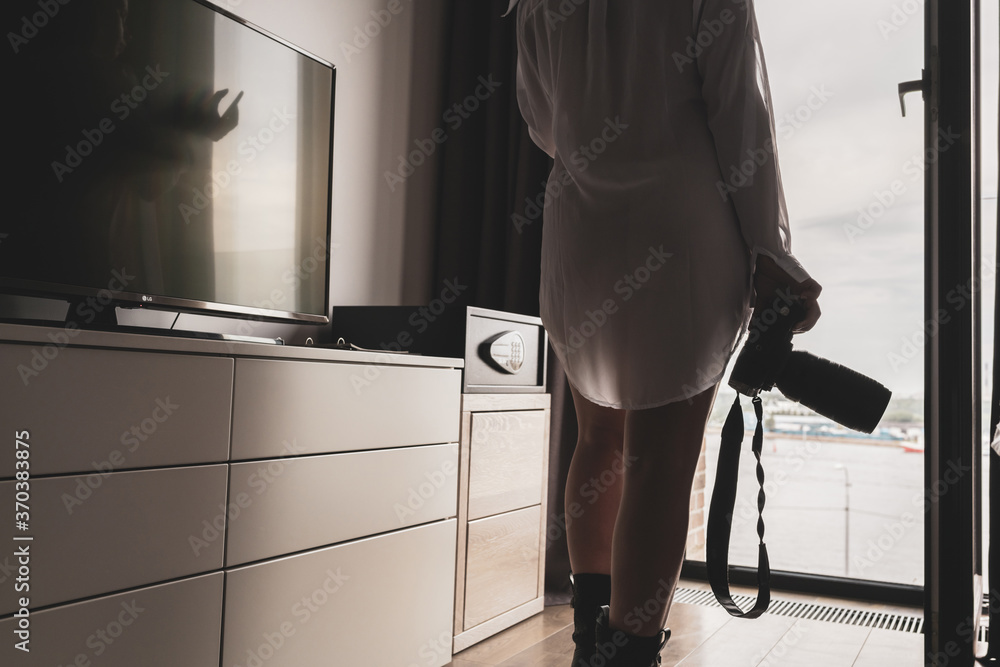 Φωτογραφία Back view of silhouette woman photographer in a transparent nightgown taking picture using camera standing near open panoramic window of apartments