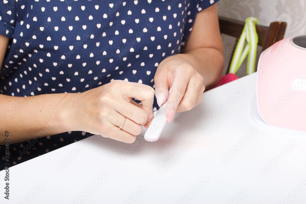 A woman makes her own manicure. Removes old nail Polish with a nail buff. Taken in close-up.
