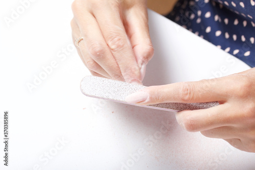 A woman makes her own manicure. Removes old nail Polish with a nail buff. Taken in close-up.