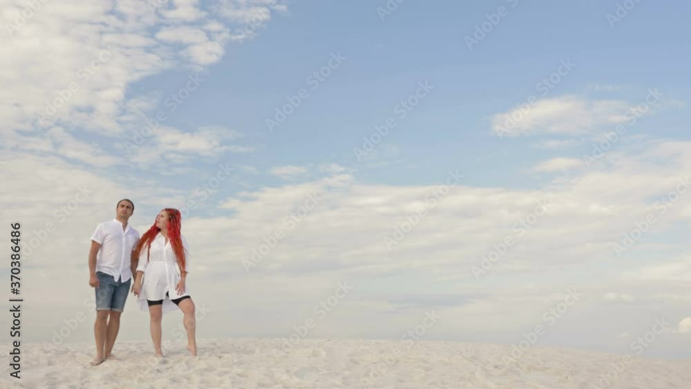 Couple in love stand on white sand against the blue sky in white clouds. Romantic date. Couple in love stand on white sand against the blue sky in white clouds. Romantic date.