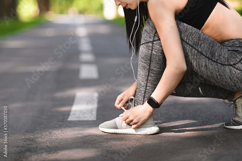 Sporty girl tying shoes laces before running, getting ready for jogging outdoors