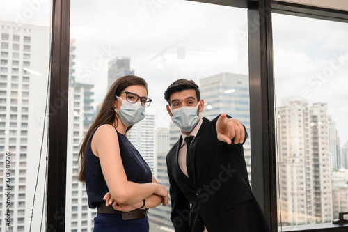 Young caucasian business colleague wearing face mask and pointing finger in modern office