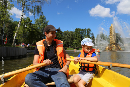 VDNKh, Exhibition of Achievements of National Economy, fountain Zolotoy Kolos, Golden Spike. Dad, son on boat in pond in Moscow city, Russia. Summer active recreation