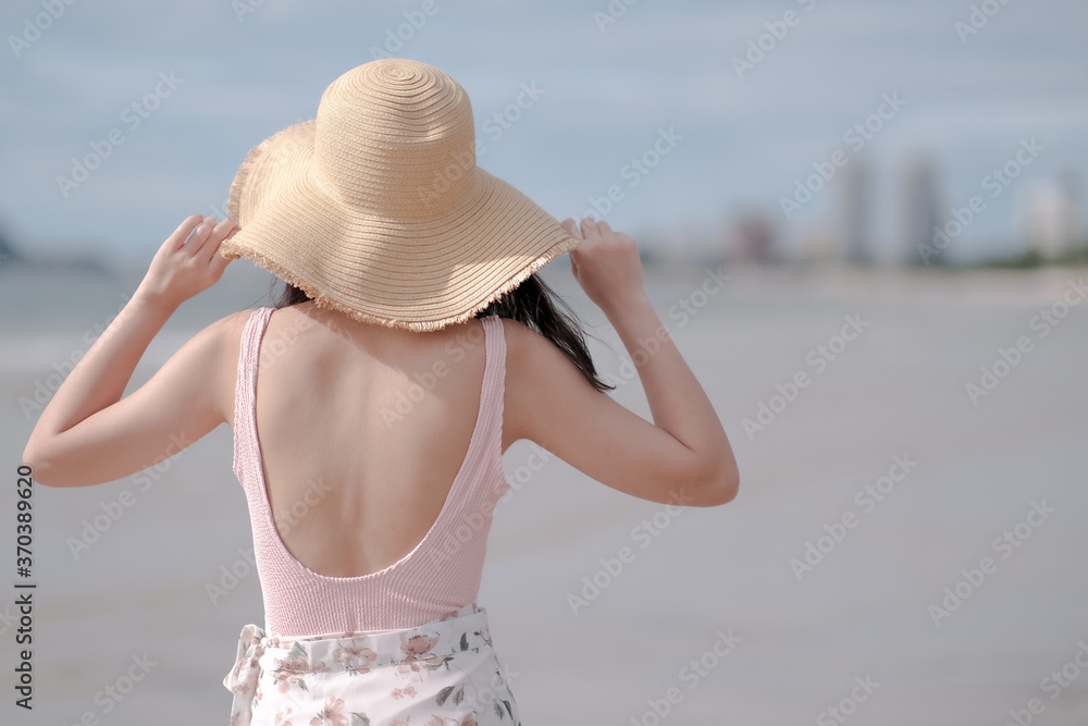 Asian girl wearing pink bodysuit and straw hat on the beach