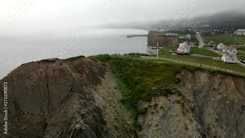 White Cross Situated On The Tip Of Gaspe Peninsula With Tourists Admiring The Calm Waters Of Saint Lawrence Gulf Near The Perce Rock in Quebec, Canada.  -aerial drone photo