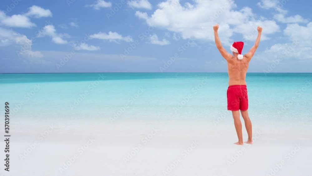 Christmas CINEMAGRAPH - seamless loop: Beach man happy on travel vacation wearing santa hat happy on beach holidays happy cheering arms raised winning celebrating on sand on travel destination. Christmas CINEMAGRAPH - seamless loop: Beach man happy on travel vacation wearing santa hat happy on beach holidays happy cheering arms raised winning celebrating on sand on travel destination.