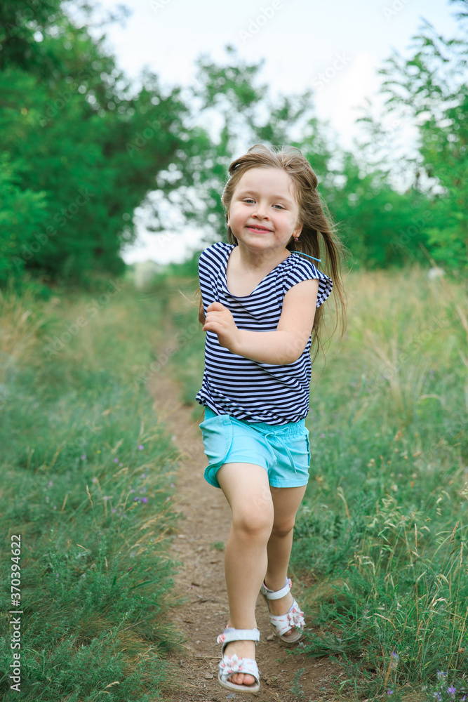 Little girl with long hair runs along the path at the edge of the forest Little girl with long hair runs along the path at the edge of the forest