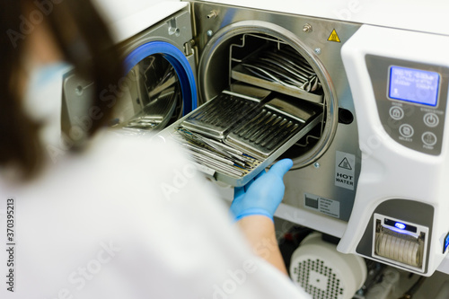 Sterilizing dental instruments in autoclave machine, over the shoulder view on hand with glove on it
