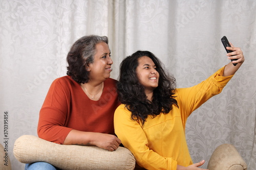 Happy looking Indian mother with her young daughter sitting on a couch or sofa. Concept Mother's day photo