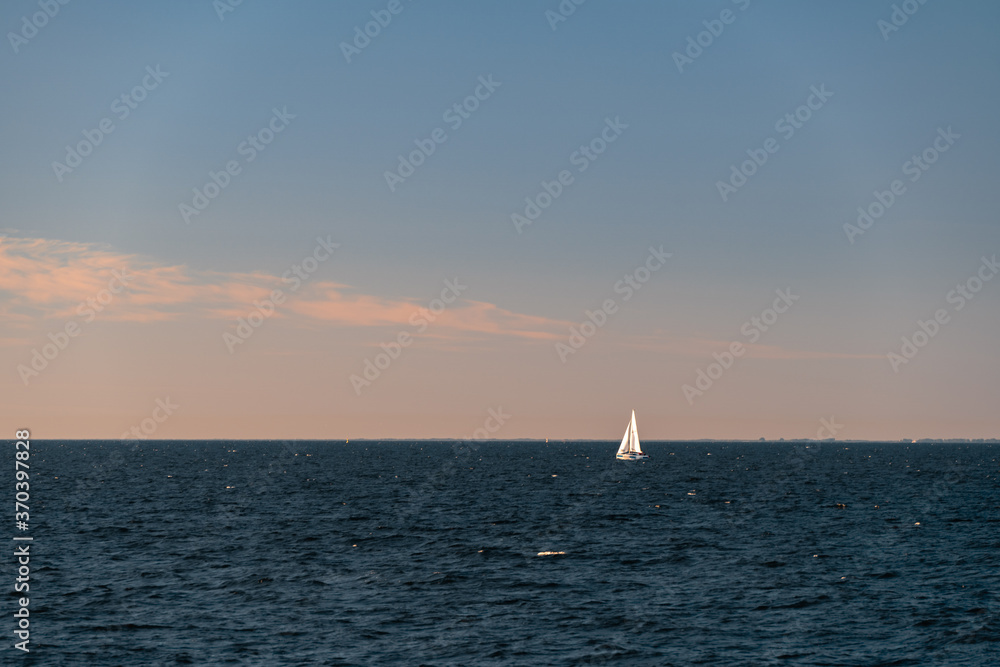 White sailboat on a calm sea or ocean during sunset. Large copy space. Minimalistic style. White sailboat on a calm sea or ocean during sunset. Large copy space. Minimalistic style.