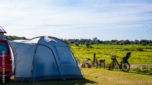 Tourist tents and car in green field at campsite. Camping place in the meadow in nature park in summer. Adventure travel active lifestyle freedom outdoors. Family time holidays.