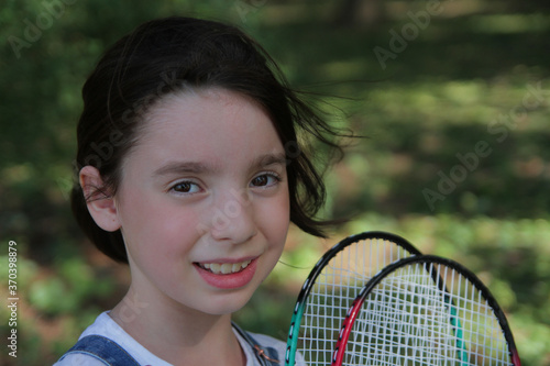  A girl on vacation in the summer in the park plays badminton with friends and parents. © miozin