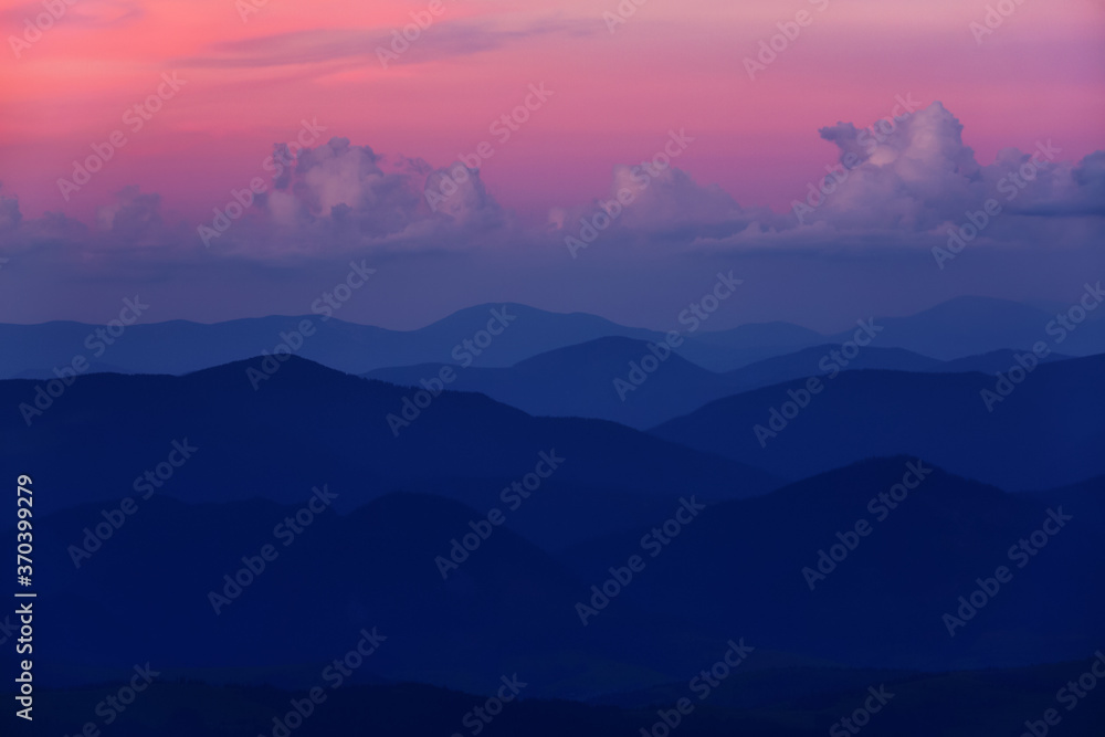 Landscape with beautiful sunset, cloudy sky and pink colorful horizon. Panoramic view. Mountain silhouette in evening. Copy space for text.