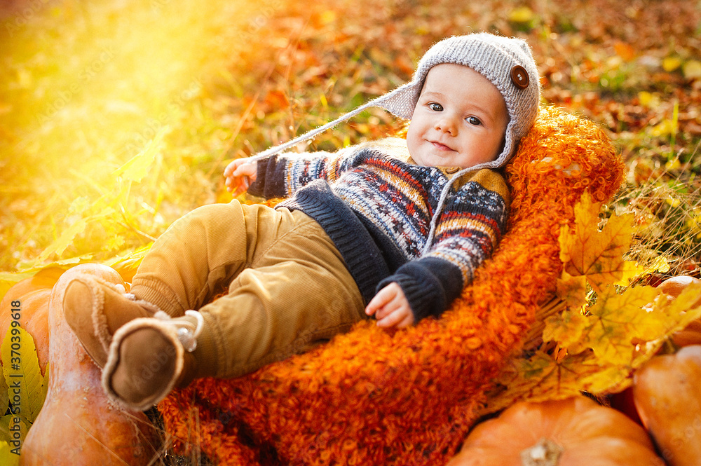 Child boy lies in a basket with pumpkins in autumn leaves.