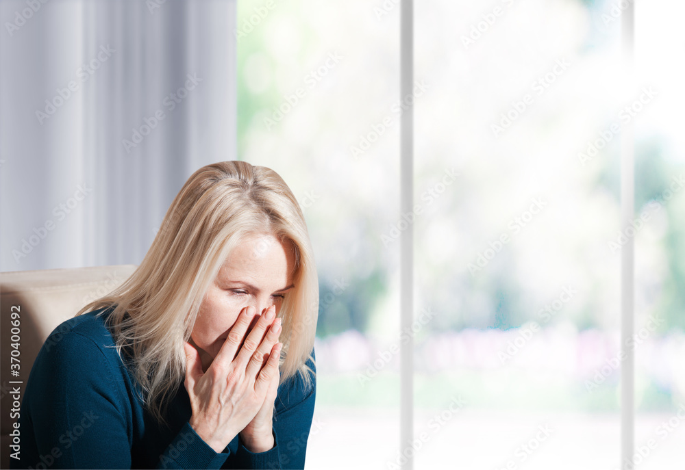 Woman suffering from stress or a headache grimacing in pain. Sad depressed woman at home sitting on the couch, looking down and touching her forehead. Woman suffering from stress or a headache grimacing in pain. Sad depressed woman at home sitting on the couch, looking down and touching her forehead.