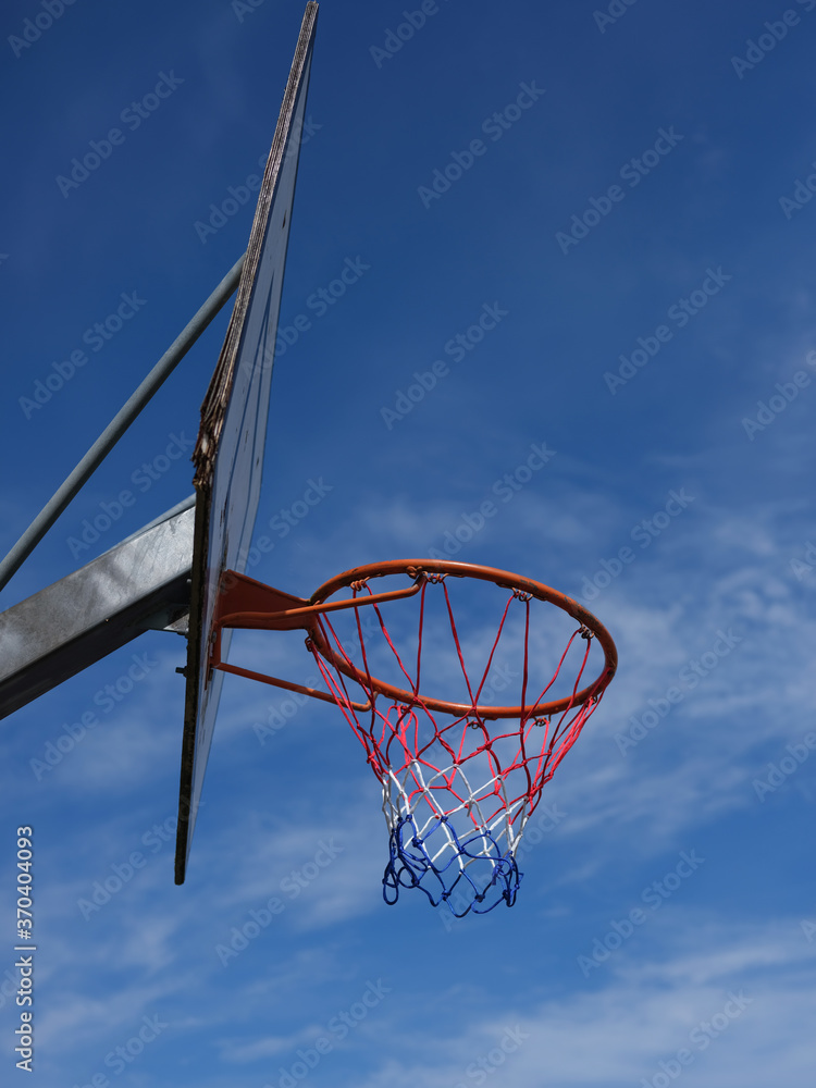 Basket hoop outside on a sunny day against a blue sky. Part of a building is shown in the background Basket hoop outside on a sunny day against a blue sky. Part of a building is shown in the background