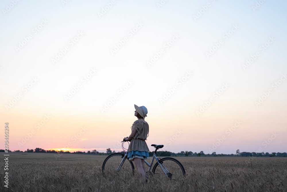 Young woman with hat ride on the bicycle in summer wheat fields