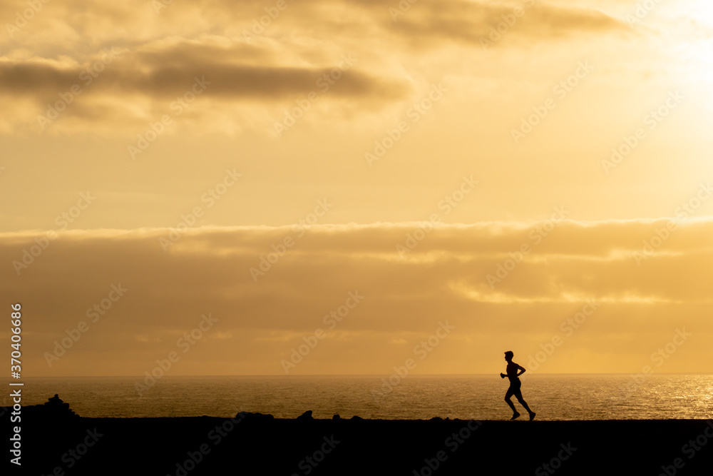 Silhouette of an unrecognizable man running in front of the sea at sunset on Lanzarote, Canary Islands, Spain. Health care and outdoor exercise concept.