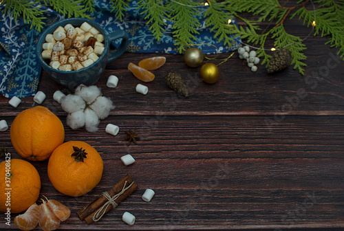 Tangerines, spruce branches, marshmallows, garlands, cinnamon sticks in the form of a Christmas composition on a dark wooden background.