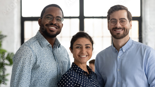 Head shot portrait smiling successful diverse employees team standing in modern office, happy overjoyed Indian businesswoman, African American and Caucasian businessmen looking at camera