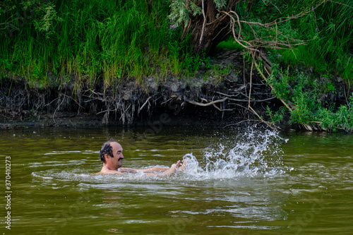 Senior man swimming in the taiga Siberian river Vagai, Russia.