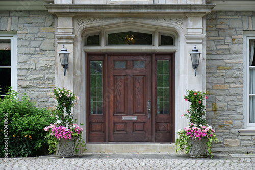 Elegant wooden front door with sidelights, with floral decorations, on stone faced house