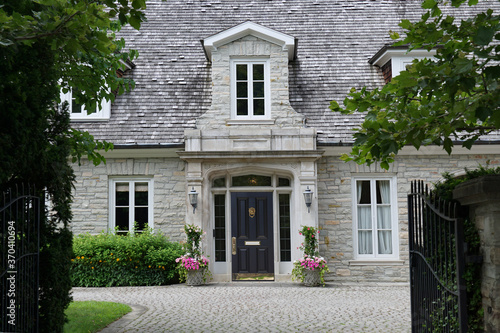 Elegant gated entrance to stone house  with dormer window and cedar shingle roof