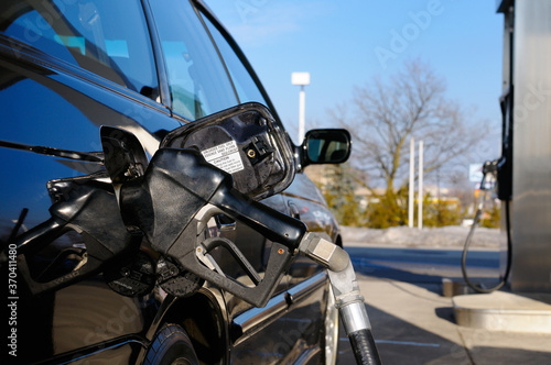 Gas pump nozzle inserted into a black car while refueling at a gas station in winter