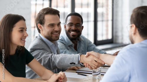 Smiling business people shaking hands, diverse people sitting at table in modern boardroom, two confident businessmen handshake, making deal, greeting and acquaintance at group negotiations