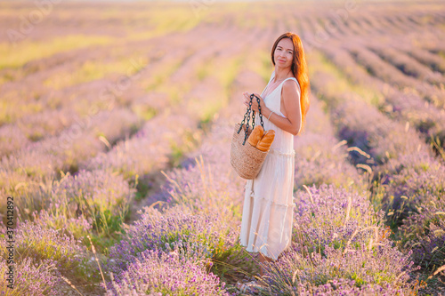 Fototapeta Naklejka Na Ścianę i Meble -  Woman in lavender flowers field at sunset in white dress and hat