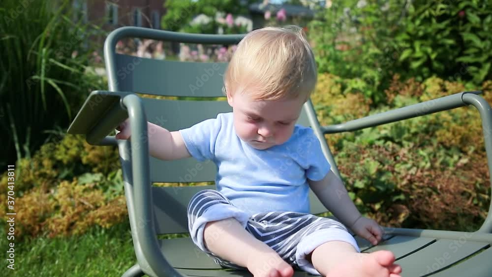 Funny baby sitting on a summer chair in the garden. Outdoors in the street Funny baby sitting on a summer chair in the garden. Outdoors in the street