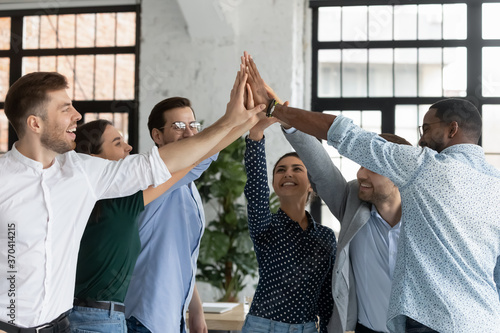 Overjoyed successful young diverse employees giving high five at corporate meeting, celebrating business achievement, teamwork result, happy colleagues engaged in team building activity, unity photo