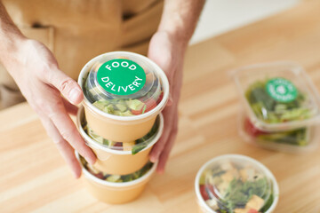 High angle close up of unrecognizable man wearing apron packaging orders while standing by wooden tables, food delivery service worker , copy space
